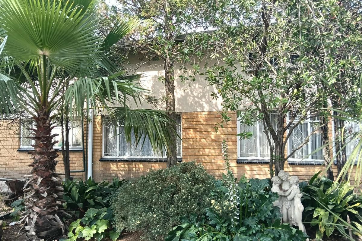 Rear exterior view of the apartment building featuring a brick facade, established garden landscaping, and security bars on the windows.