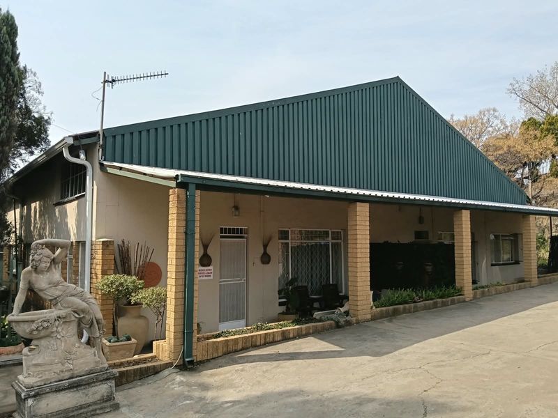 Front elevation of the property featuring a large corrugated metal roof, covered patio area with brick pillars, and a concrete driveway.