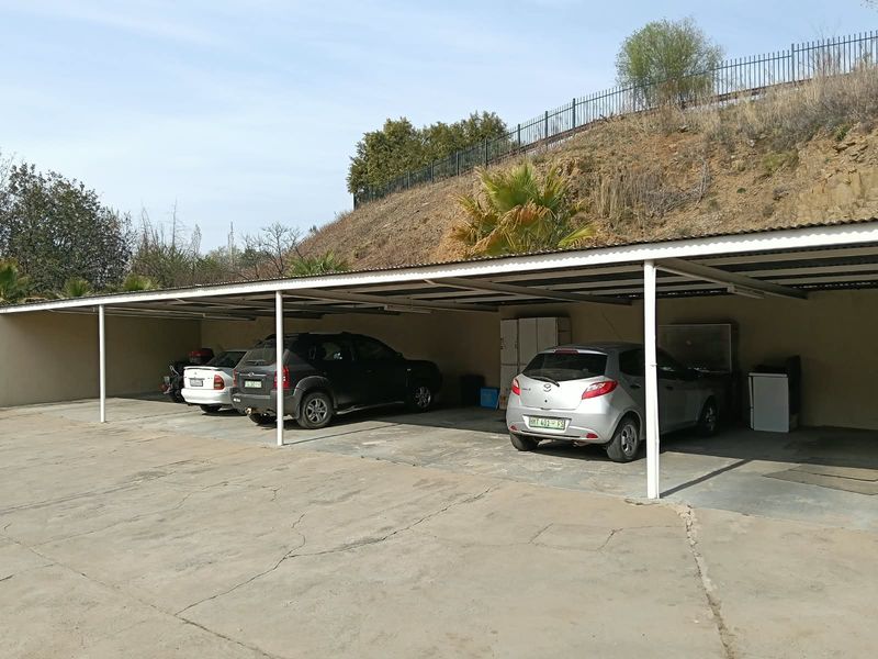 Covered carport area with concrete paving and metal roofing, providing sheltered parking spaces for multiple vehicles.