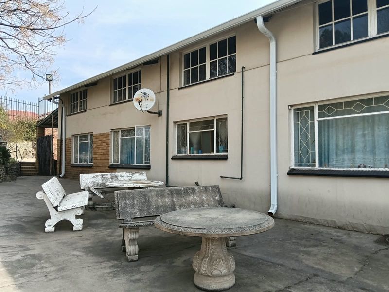 Rear exterior view of the apartment building featuring a concrete patio area, multi-pane windows with security bars, and a satellite dish installation.