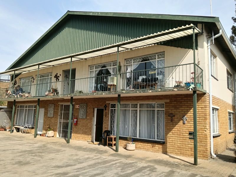Front elevation of a two-story apartment building featuring a brick facade, a full-length upper balcony with metal railings, and a concrete driveway.