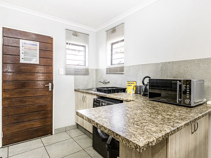 A functional kitchen area featuring laminate countertops, tiled backsplash, built-in cabinetry, and tiled flooring with direct access to an exterior door.