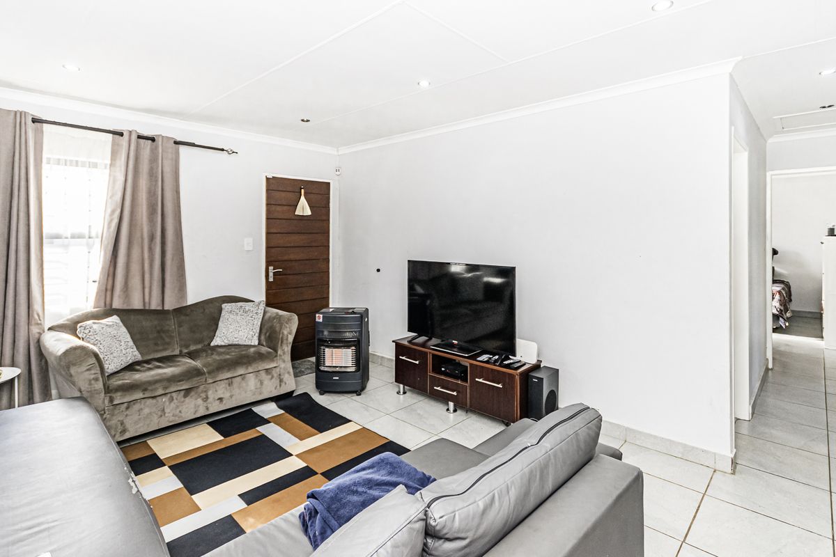 A functional living room featuring tiled flooring, recessed downlights, and coved ceilings, providing a neutral base for potential interior updates.