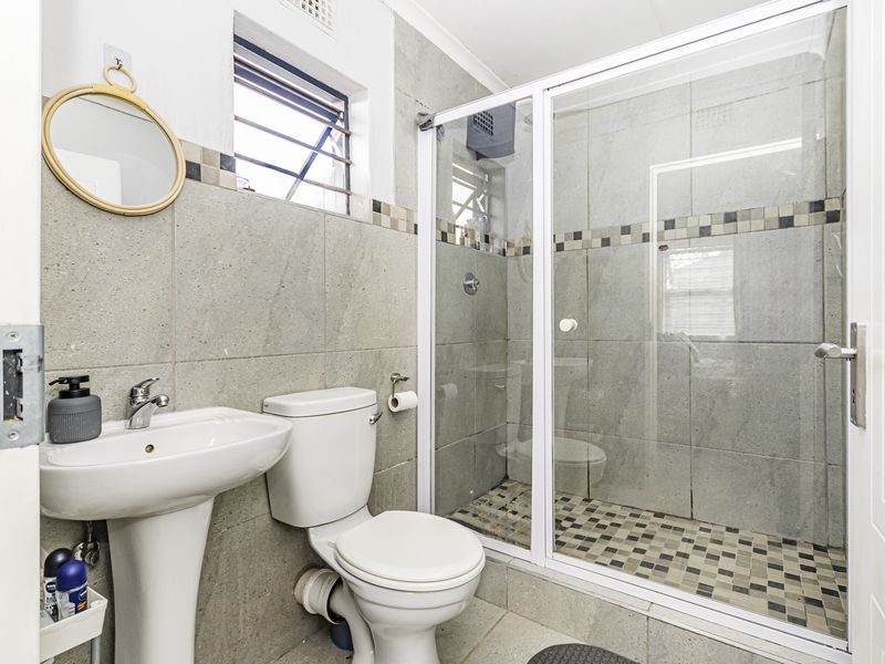 A functional bathroom featuring a pedestal basin, toilet, and a glass-enclosed shower with neutral wall and floor tiling.