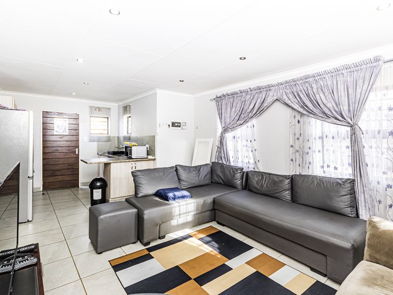 An open-plan living area featuring tiled flooring, recessed lighting, and a compact kitchen space with built-in cabinetry and countertops.