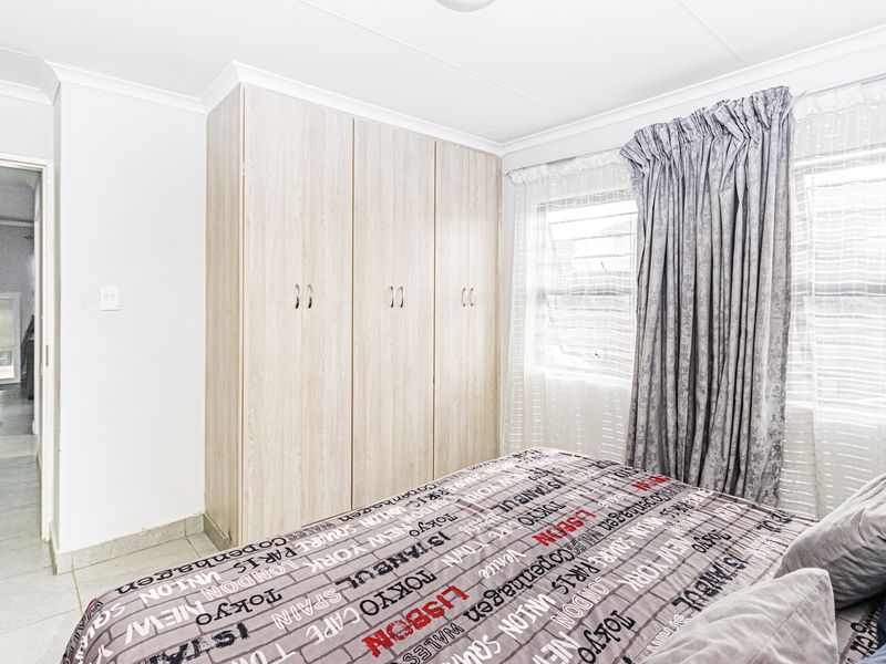 A bedroom featuring light wood-finish built-in cupboards, tiled flooring, and decorative coving, with a view into the adjacent hallway.