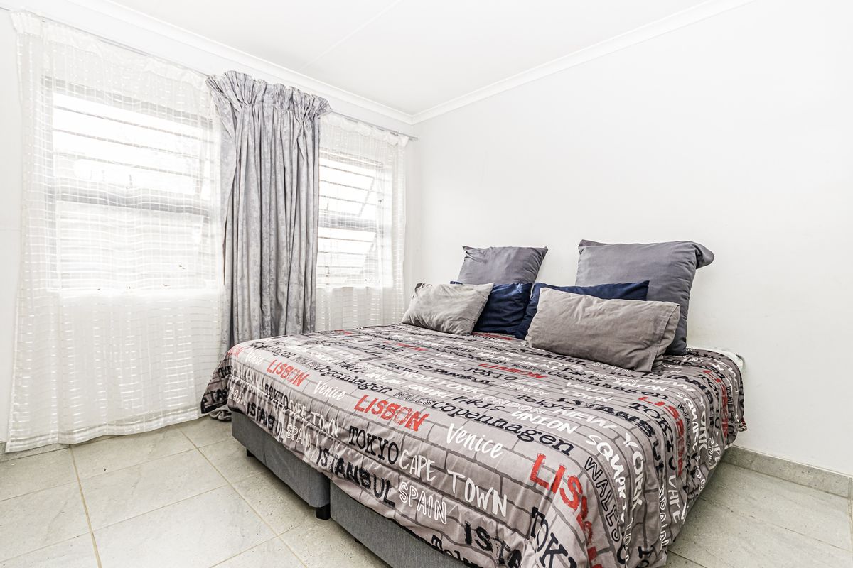 A bedroom featuring tiled flooring and large windows with curtain rails, providing a bright and functional living space.