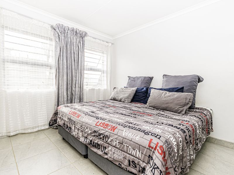 A bedroom featuring tiled flooring and large windows with curtain rails, providing a bright and functional living space.