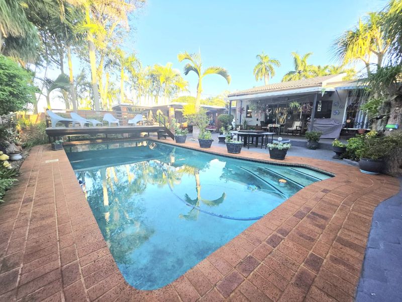 Outdoor pool area featuring a swimming pool with brick coping, a raised timber deck, and an adjacent covered patio space.