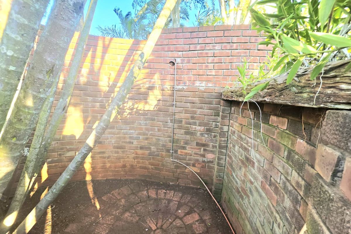 An outdoor shower area featuring a curved brick wall and circular brick paving, set within a garden environment.