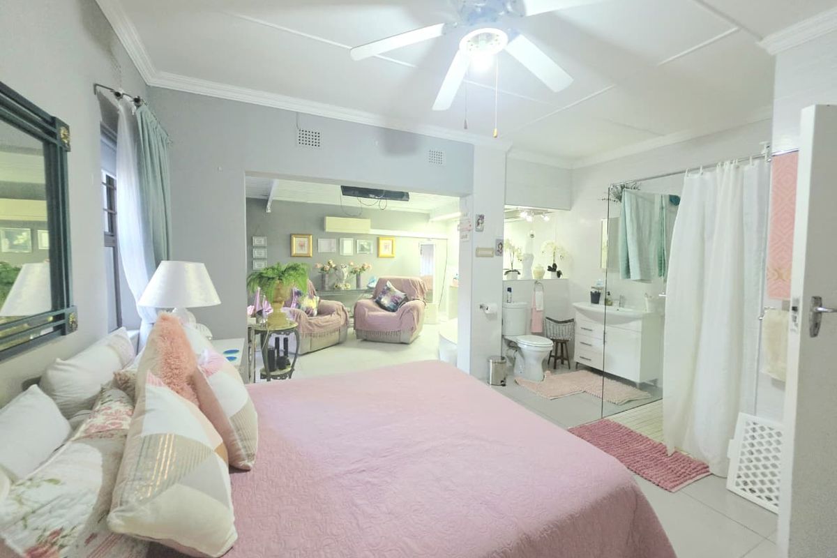 Spacious bedroom featuring an integrated en-suite bathroom with a vanity, toilet, and glass-enclosed shower area, complemented by a ceiling fan.