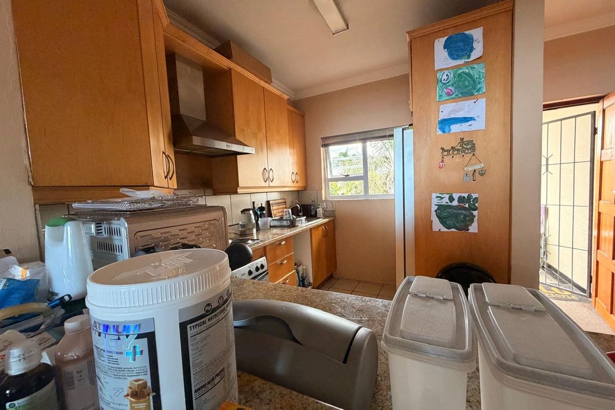 A functional kitchen featuring wooden cabinetry, granite countertops, and an integrated extractor fan, with direct access to an exterior area via a security gate.