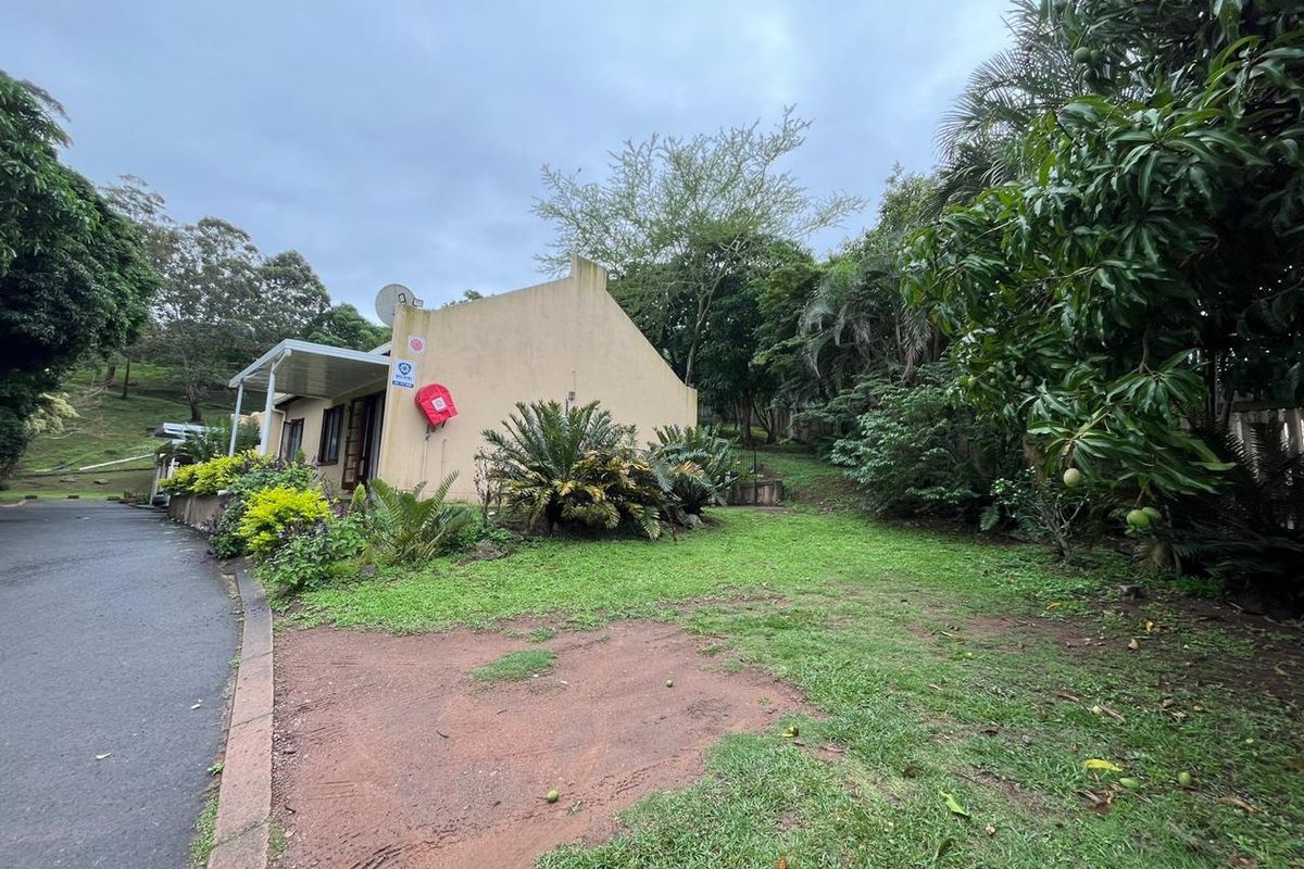 Rear view of the townhouse featuring a covered patio area, adjacent lawn, and established garden surroundings.