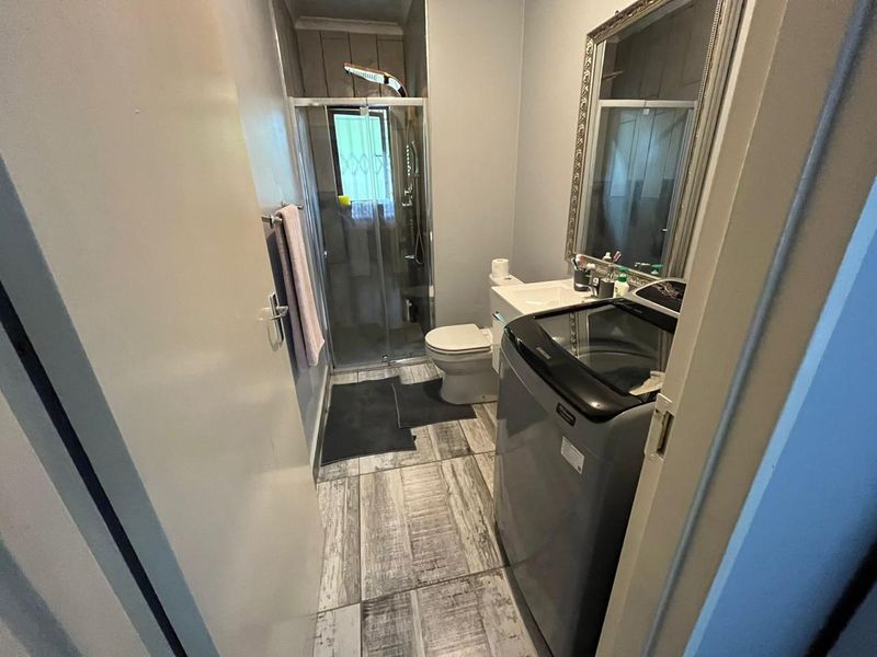 A functional bathroom featuring a shower enclosure, toilet, and vanity basin with modern wood-look floor tiles.