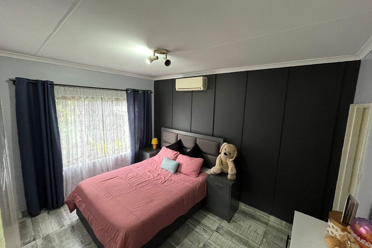 A well-maintained bedroom featuring tiled flooring, a split-system air conditioner, and a dark feature wall with integrated built-in wardrobe cabinetry.