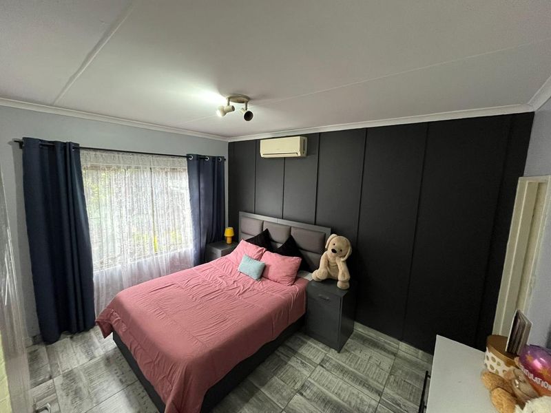 A well-maintained bedroom featuring tiled flooring, a split-system air conditioner, and a dark feature wall with integrated built-in wardrobe cabinetry.
