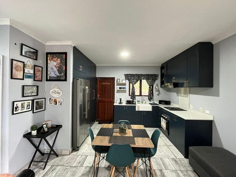 An open-plan kitchen and dining area featuring modern dark blue cabinetry, a farmhouse sink, built-in appliances, and tiled flooring.