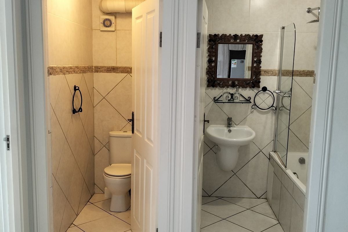 A functional bathroom layout featuring a separate toilet cubicle and a main bathroom area with a pedestal basin, bathtub, and glass shower screen.