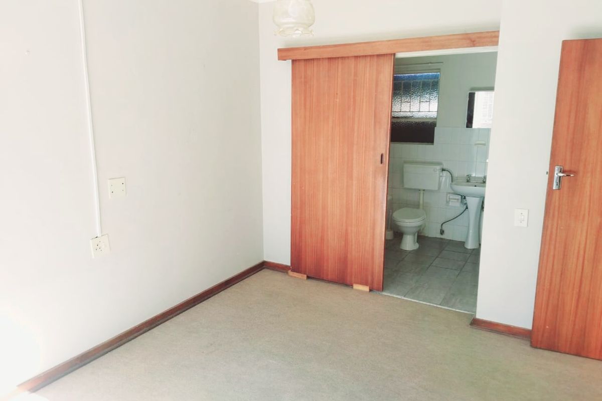 An empty bedroom featuring carpeted flooring, a sliding wooden door providing access to an en-suite bathroom, and surface-mounted electrical conduit.
