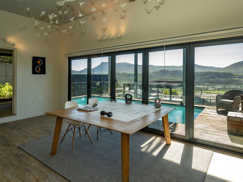 Spacious living area featuring large aluminium sliding doors that open onto a deck with a swimming pool and scenic mountain views.