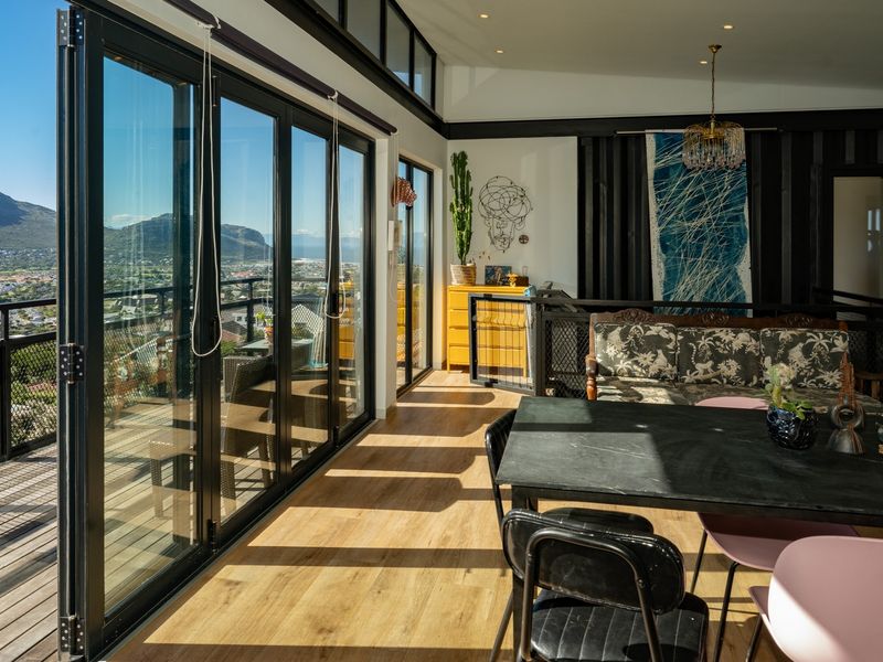 Spacious living area featuring expansive bi-fold glass doors that open onto a timber deck, offering panoramic mountain and valley views with abundant natural light.