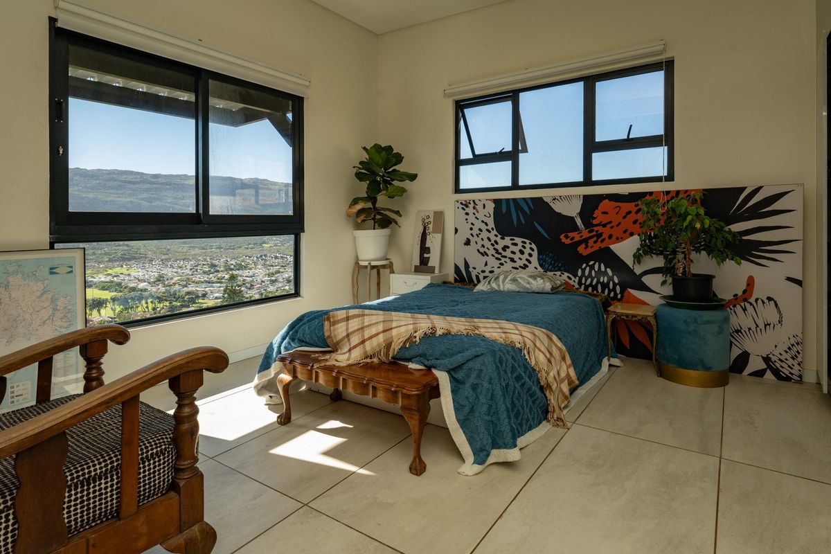 A bright bedroom featuring large aluminium-framed windows with scenic mountain and valley views, tiled flooring, and a built-in wardrobe.