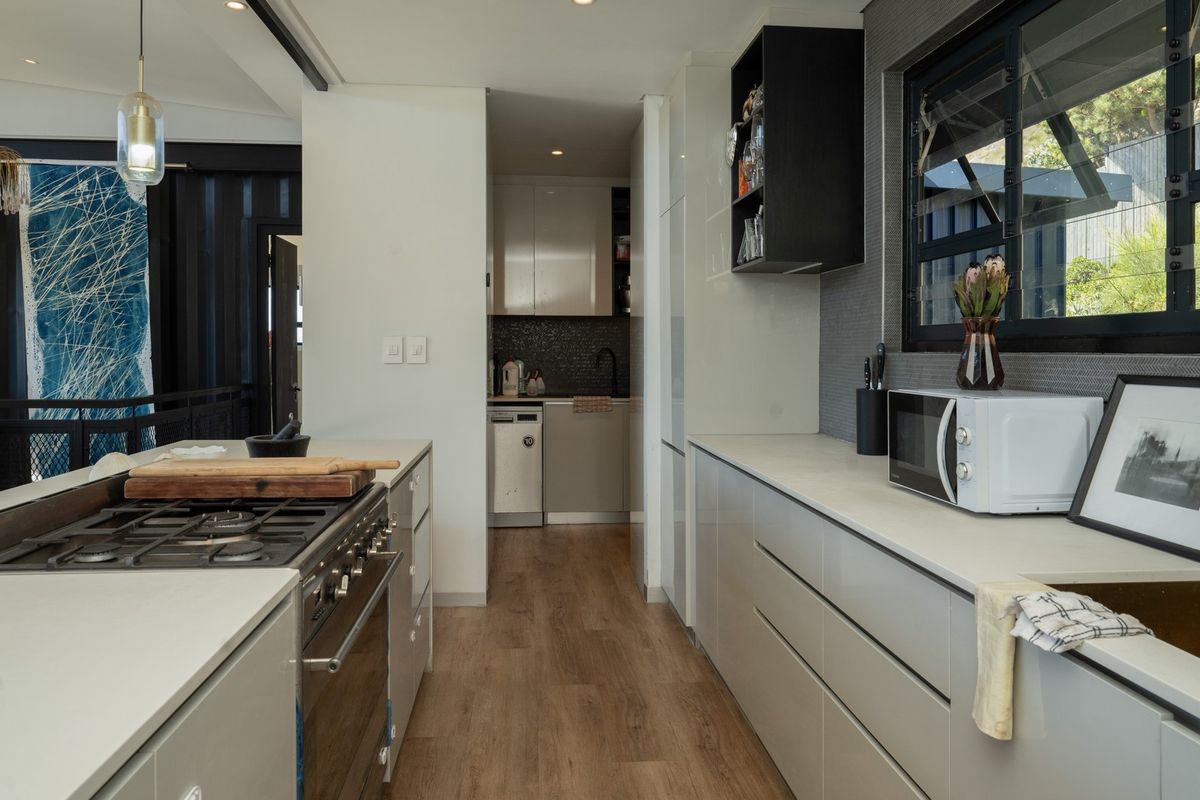 Modern kitchen featuring sleek cabinetry, stone countertops, a gas cooktop, and a functional scullery area with high-quality finishes and contemporary lighting.