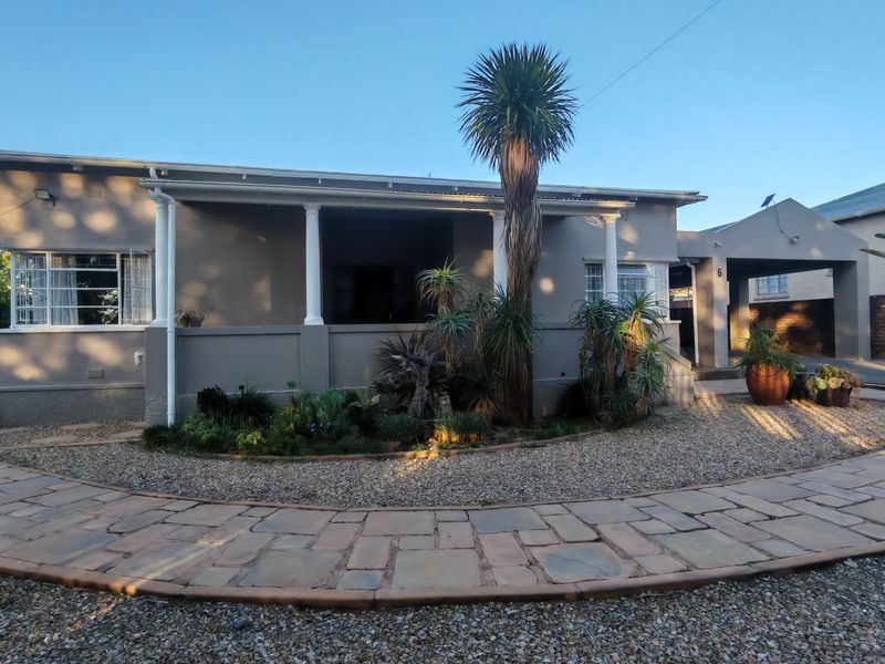 Front elevation of a single-story house featuring a covered veranda, columns, and a paved walkway leading to a carport.
