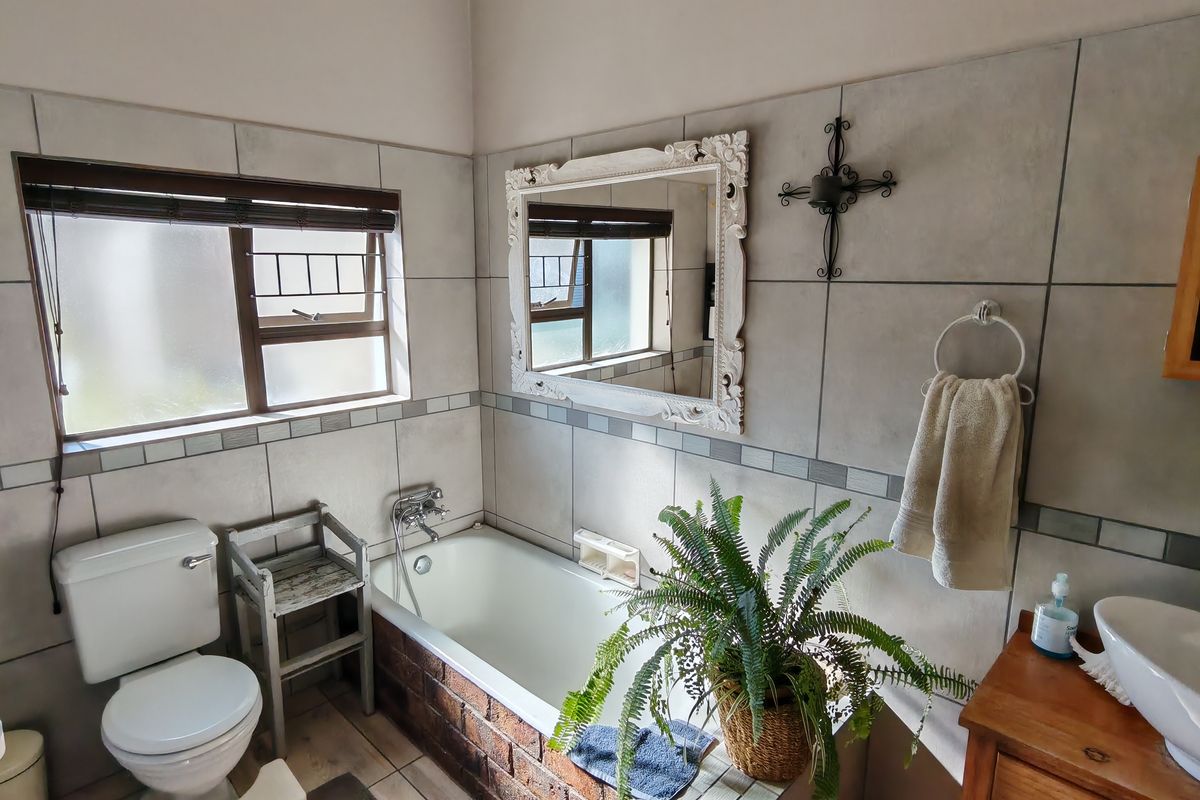 A functional bathroom featuring a built-in bathtub, ceramic wall tiling, a standard toilet, and a basin with a wall-mounted mirror.