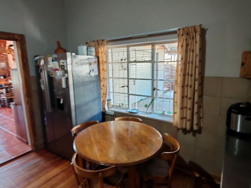 A functional kitchen area featuring wooden flooring, tiled splashbacks, and a steel-framed window with security bars, leading into an adjacent living space.
