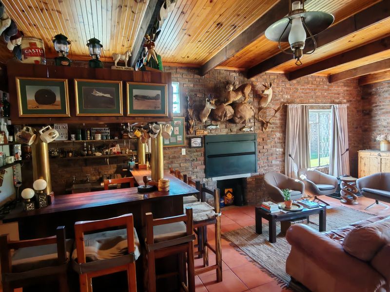 A rustic bar area featuring exposed brick walls, timber-clad ceilings with exposed beams, a built-in bar counter, and a fireplace.