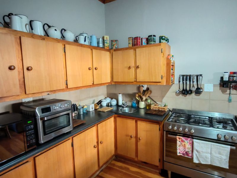 A functional kitchen featuring wooden cabinetry, a gas stove, stainless steel sink, and tiled backsplash with wooden flooring.
