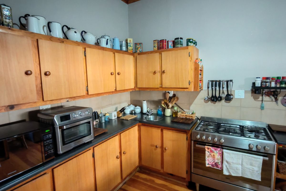 A functional kitchen featuring wooden cabinetry, a gas stove, stainless steel sink, and tiled backsplash with wooden flooring.