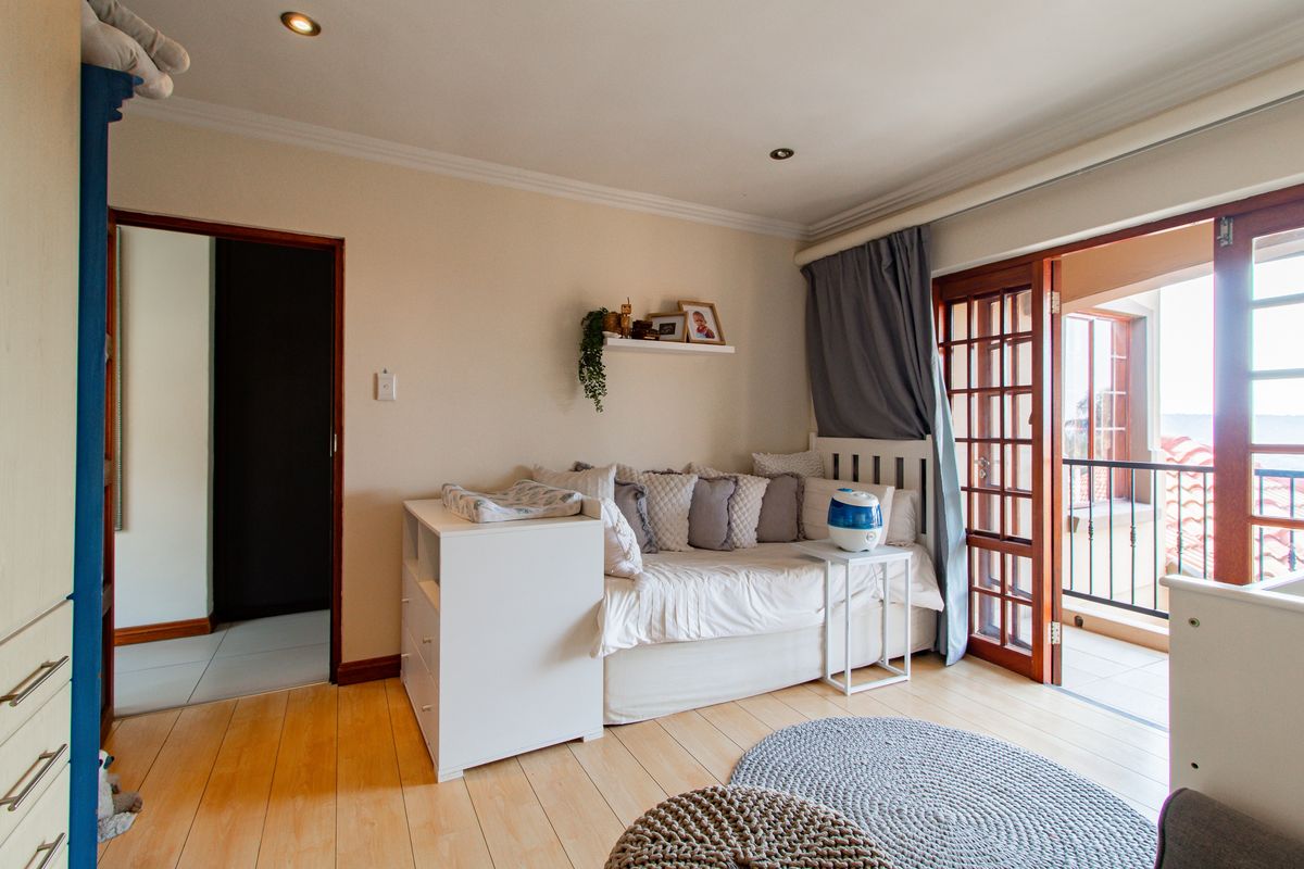 A well-lit bedroom featuring light wood flooring, recessed ceiling lighting, and direct access to a private balcony through wooden framed glass doors.