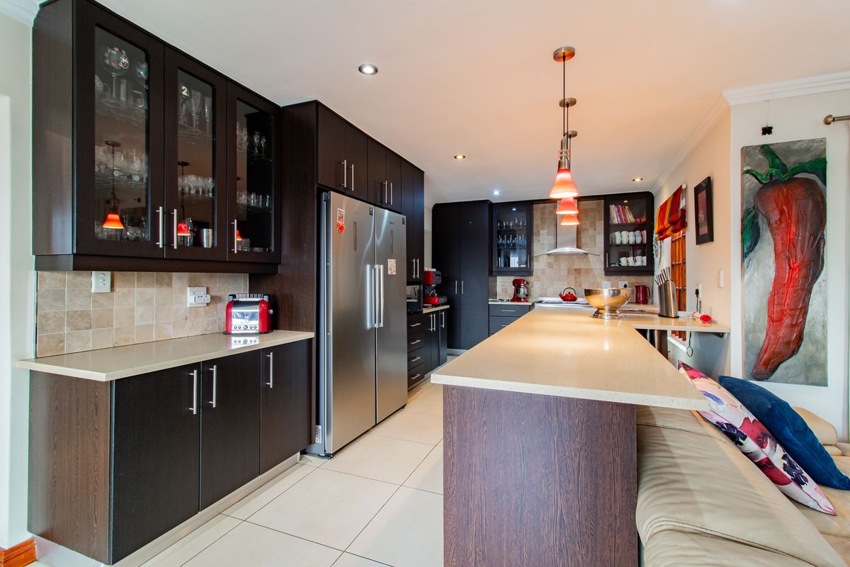 Modern kitchen featuring dark wood cabinetry, stone countertops, a large central island with breakfast bar seating, and integrated stainless steel appliances.