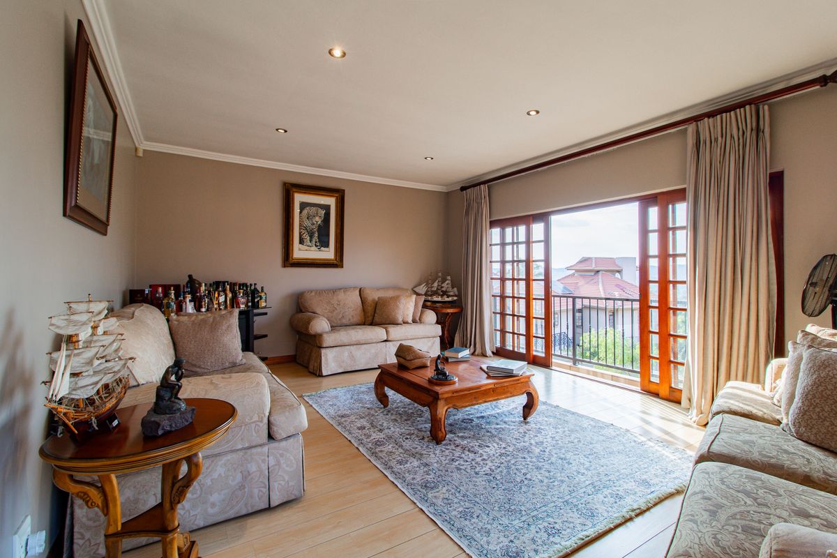 Spacious living room featuring light wood-look flooring, recessed ceiling lighting, and large wooden sliding doors opening onto a balcony with scenic views.