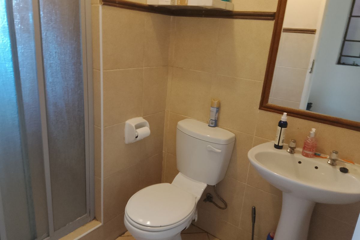 A functional bathroom featuring a pedestal basin, a standard toilet, and a shower enclosure with tiled walls.