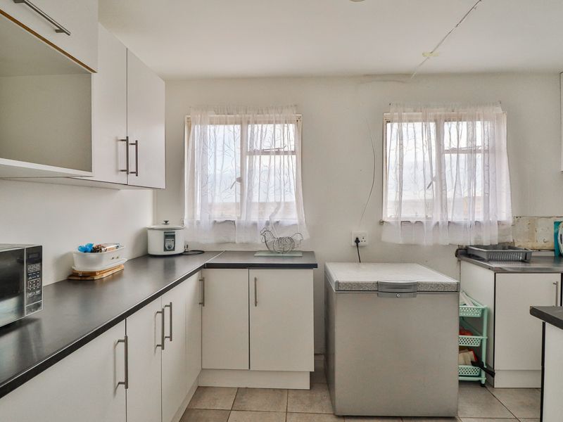 A functional kitchen featuring white cabinetry, dark laminate countertops, and tiled flooring, requiring minor cosmetic updates and ceiling repairs.