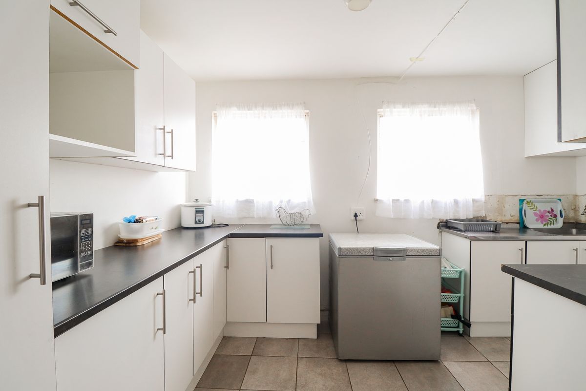 A functional kitchen featuring white cabinetry, dark laminate countertops, and tiled flooring, currently requiring minor finishing work to the backsplash area.