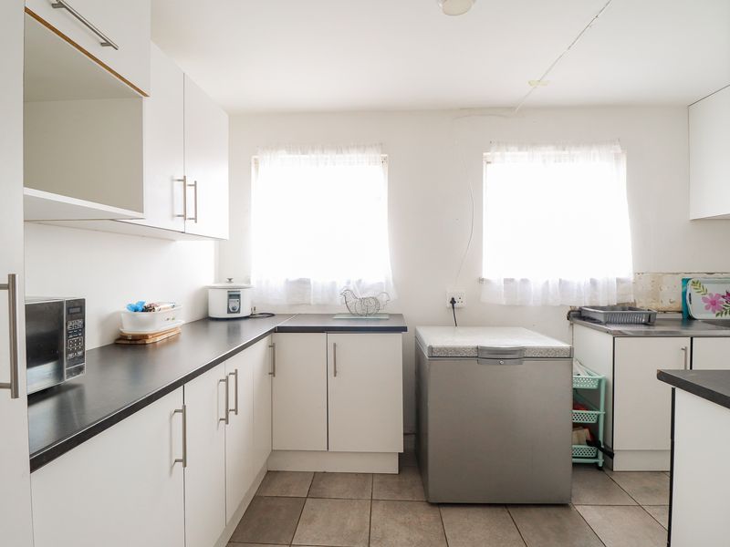 A functional kitchen featuring white cabinetry, dark laminate countertops, and tiled flooring, currently requiring minor finishing work to the backsplash area.