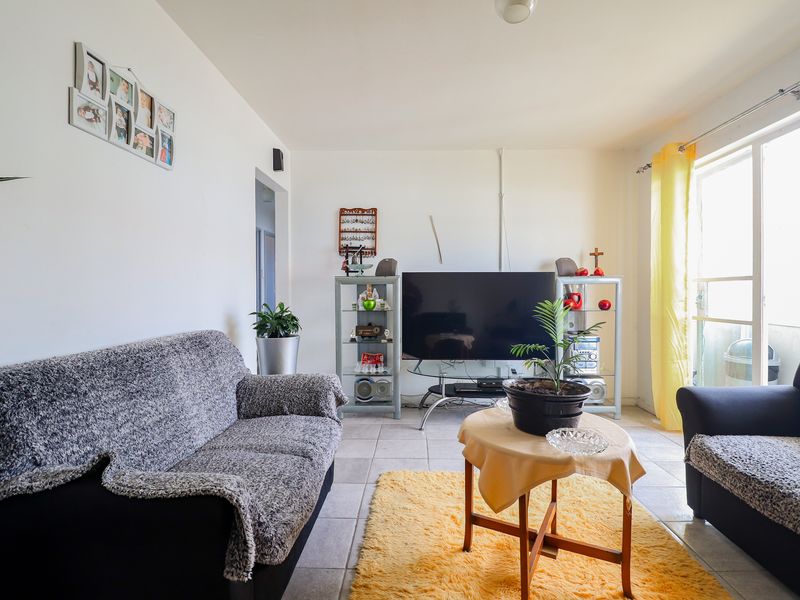 A bright living room featuring neutral tiled flooring and a large sliding glass door providing access to the balcony.