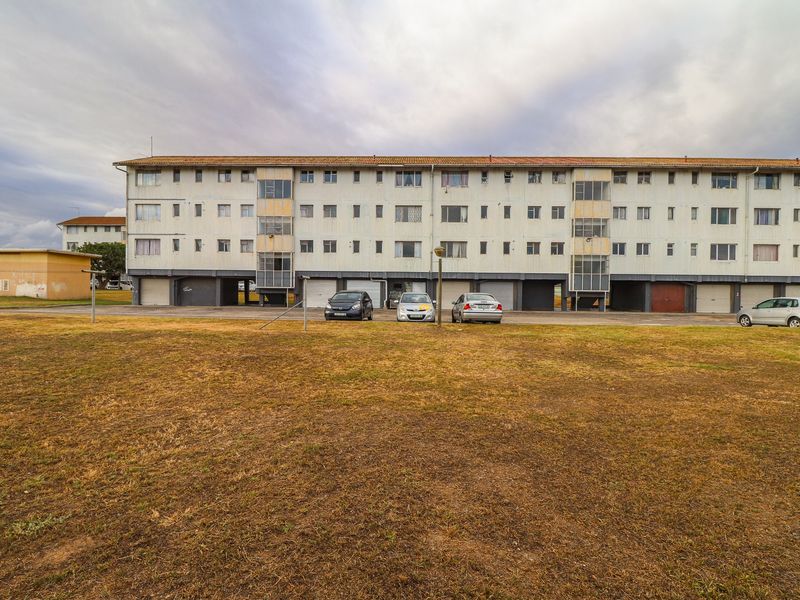 Exterior view of a multi-story apartment complex featuring ground-level garage access and a large communal lawn area.