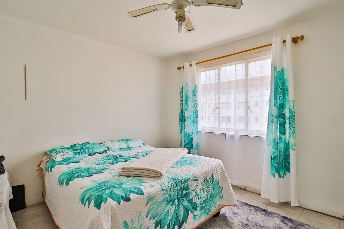 A bedroom featuring tiled flooring and a ceiling fan, with natural light provided by a window.