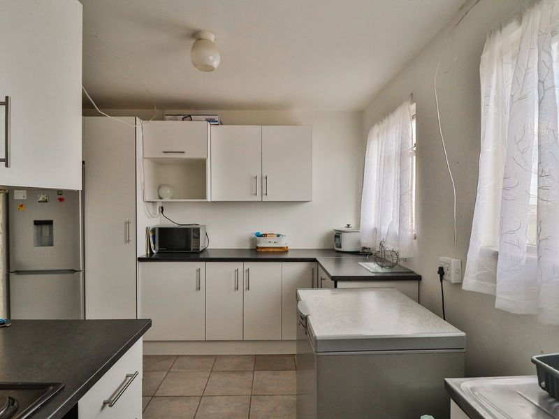 A functional kitchen featuring white cabinetry, dark laminate countertops, and tiled flooring, requiring some cosmetic updates to the wall finishes and electrical presentation.