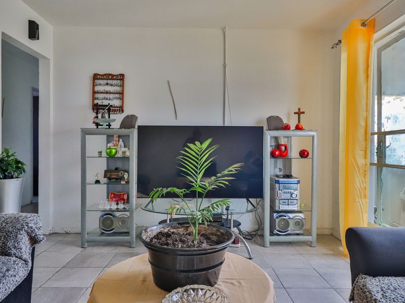 A living room featuring tiled flooring and a sliding glass door providing natural light, with visible wall-mounted wiring and standard finishes.