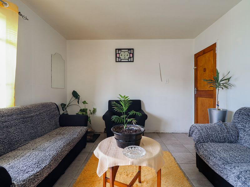 A living room featuring tiled flooring, a wooden door, and natural light from a side window.
