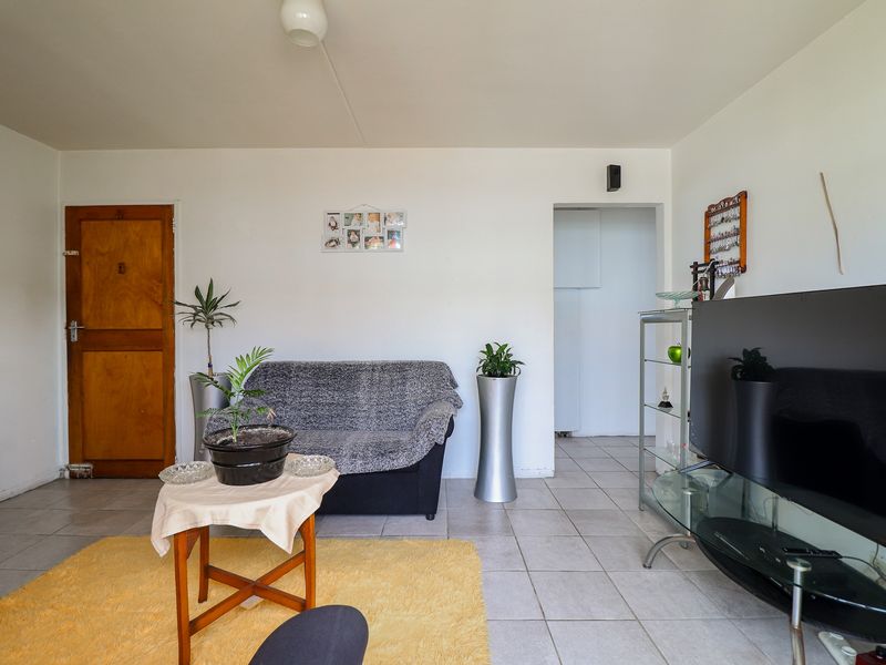 A living room area featuring tiled flooring and a wooden door, providing a functional space with neutral wall finishes.