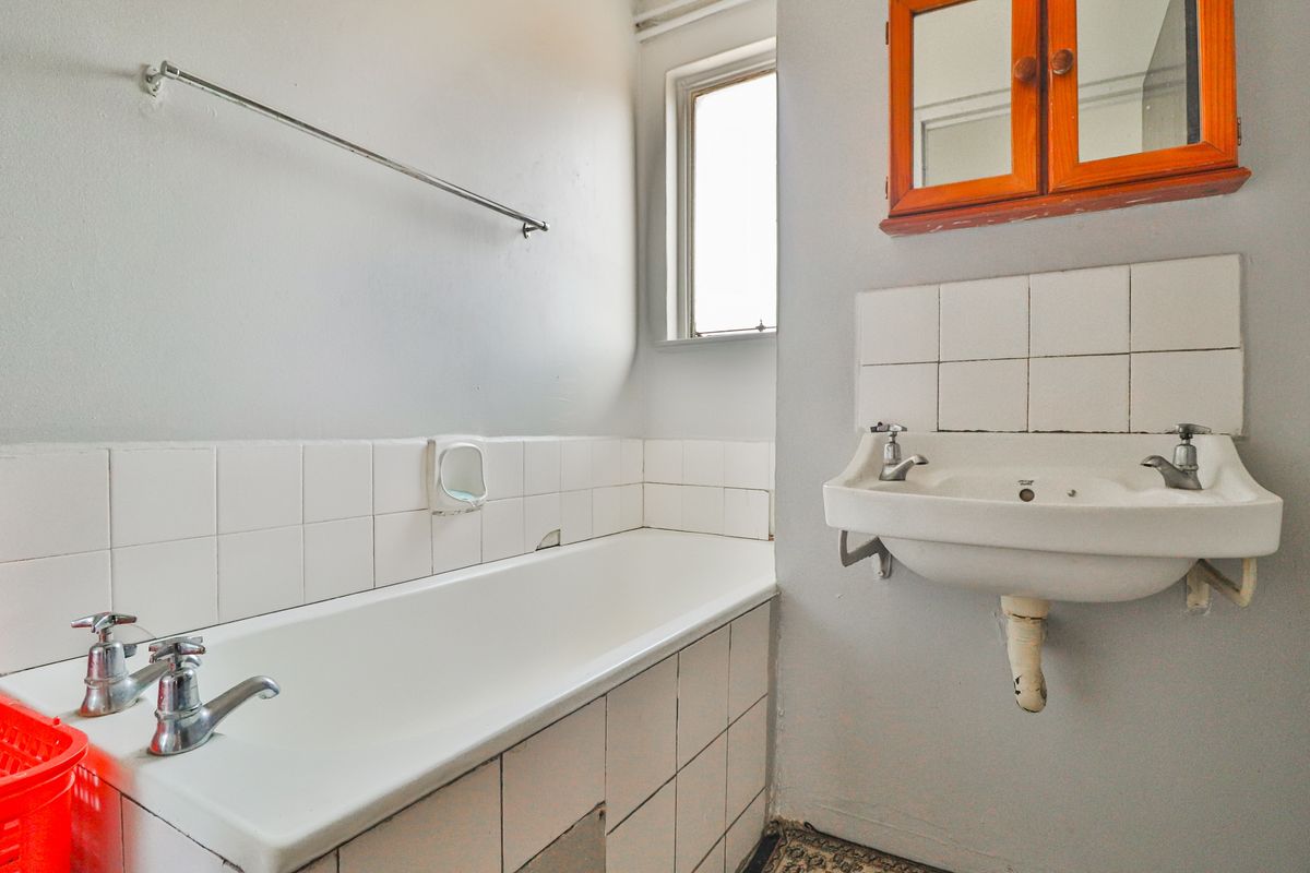 A dated bathroom featuring a standard bathtub, wall-mounted basin, and tiled splashbacks, requiring cosmetic updates to modernize the space.