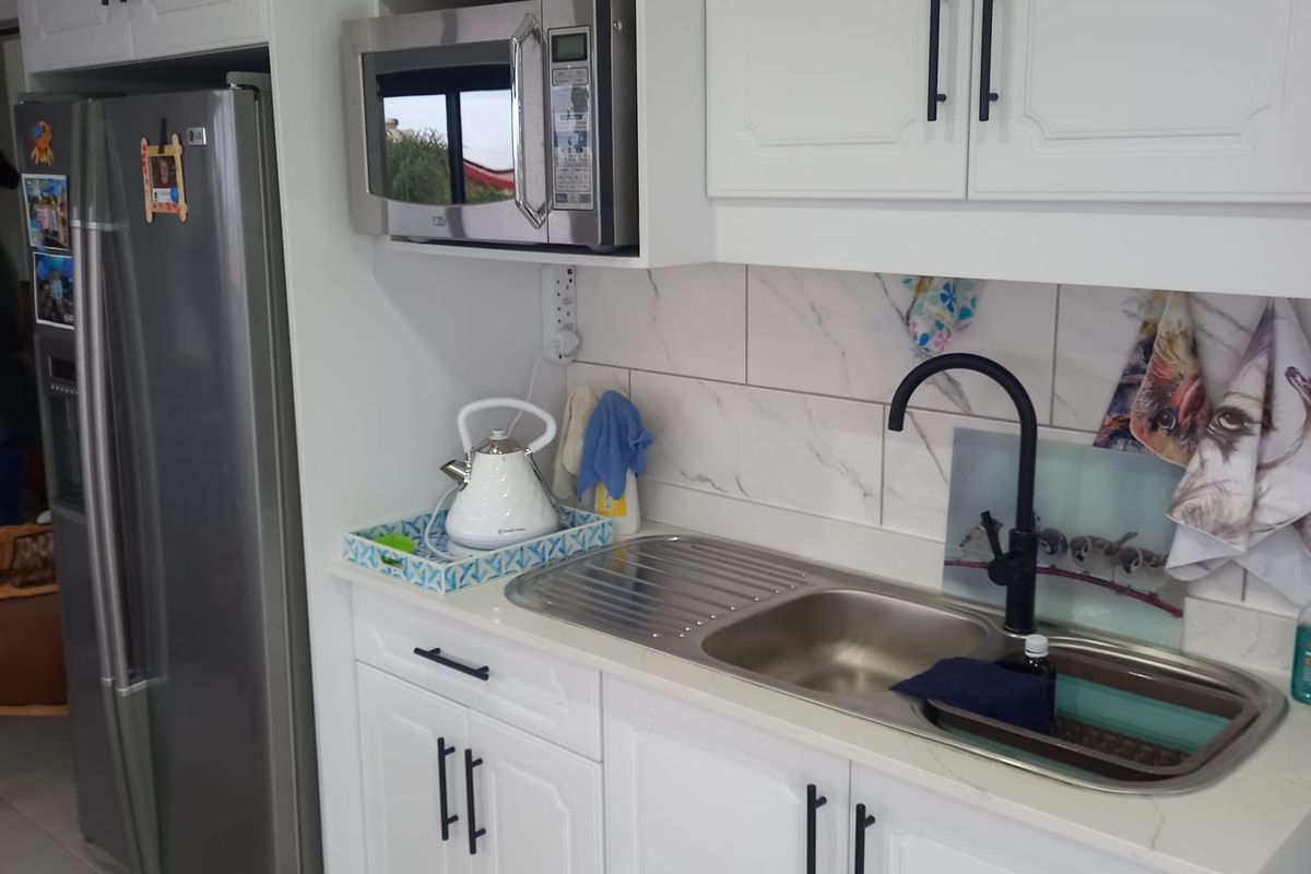A clean, modern kitchen area featuring white cabinetry, a stainless steel sink with a black tap, and a built-in microwave.