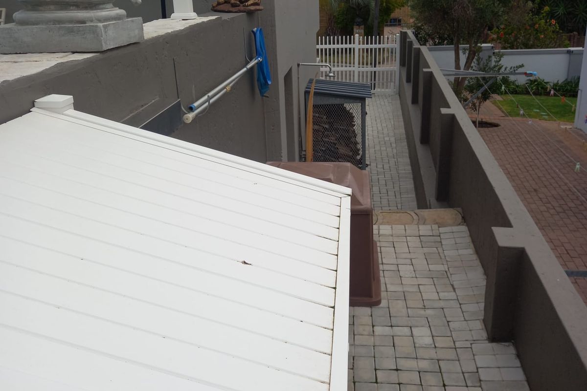 A side exterior walkway featuring paved flooring, a boundary wall, and an outdoor shower area leading towards the rear garden.